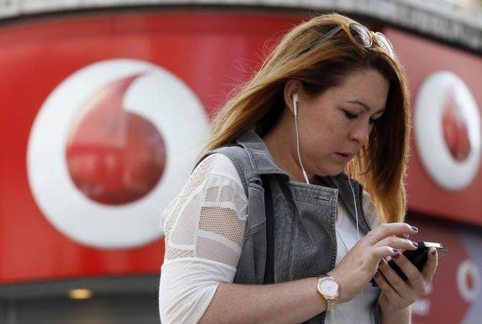 A woman talks on her mobile phone as she walks past a Vodafone store in London